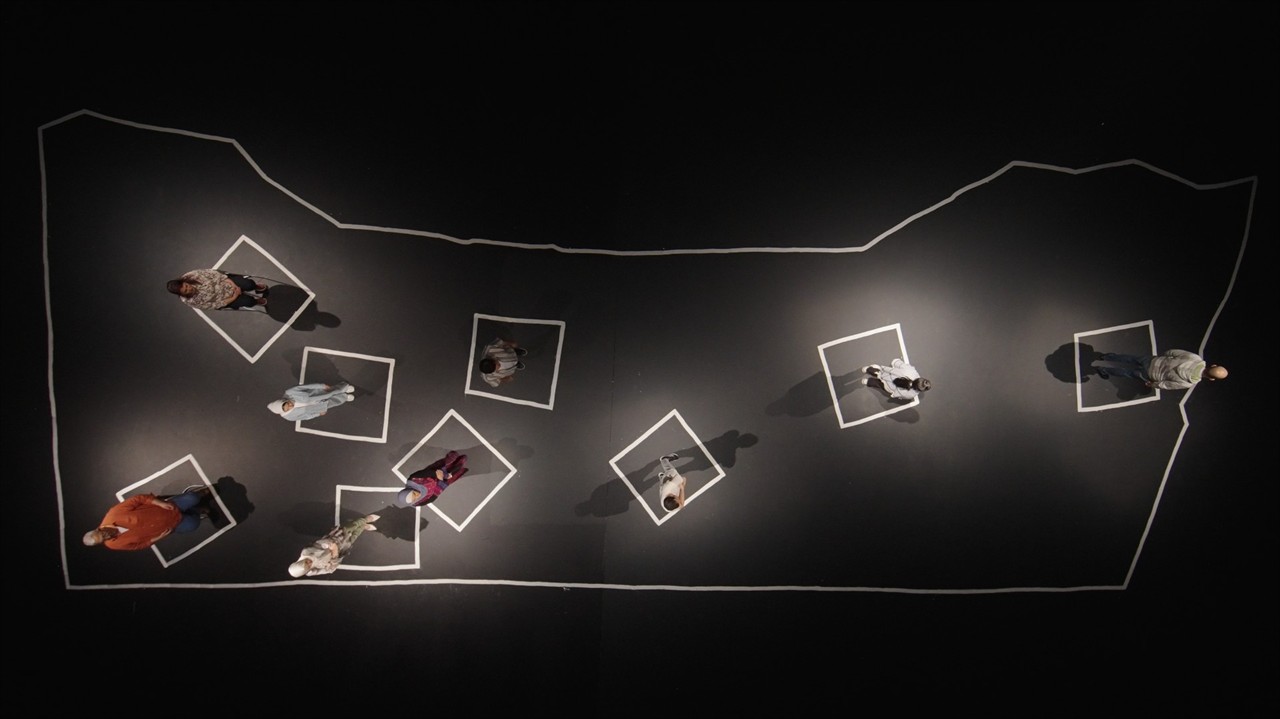 People stand in white squares on a black floor